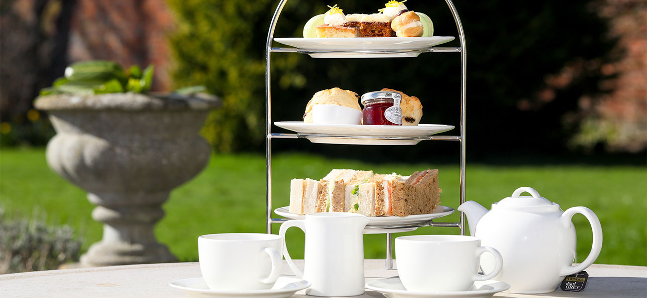 Afternoon tea stand with cakes and sandwiches, plus pot of tea on a table in the garden