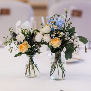 Blue, white and pale orange flowers in a small glass vase on a table