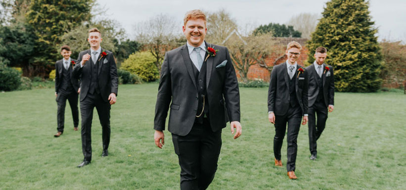 4 groomsmen and and the groom walking across the lawn in their suites