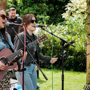 two musicians singing and playing a guitar under the pergola at the May bank holiday garden party