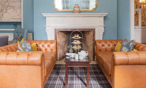 Afternoon-tea-blog Blue lounge with 2 leather sofas in front of the fireplace with afternoon tea set out on the table