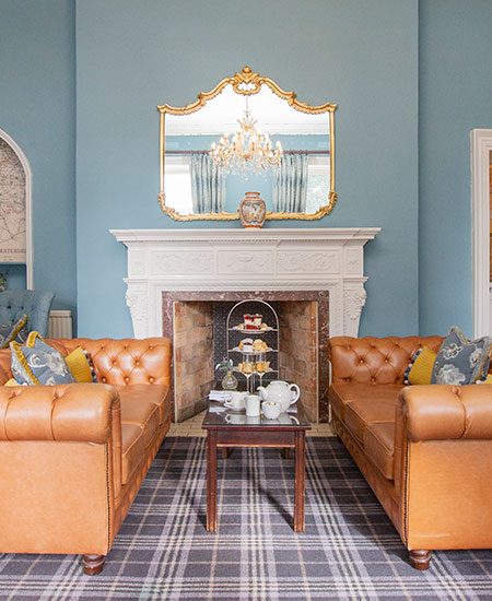 Blue lounge with 2 leather sofas in front of the fireplace with afternoon tea set out on the table